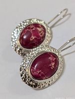 Pair of sterling silver earrings with hammered texture and oval reddish-purple gemstone centerpiece, hook ear wires.