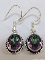 Front view of sterling silver earrings with oval faceted mystic topaz gemstones showing green and purple color shift and twisted rope silver border.