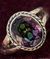 Close-up top view of mystic topaz ring showing colorful facets and twisted rope bezel setting.