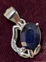 Close-up photo of the front of the sterling silver pendant showing the blue sapphire and cubic zirconia accents on a dark fabric background.