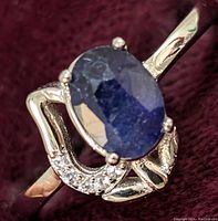 Close-up front and angle views of sterling silver ring set with oval sapphire and small clear stones on decorative band