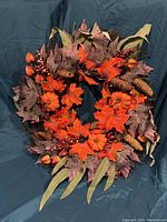 Front view of wreath showing detailed orange pumpkins, colorful autumn leaves, pine cones, and berries.
