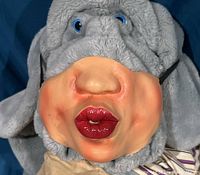 Close-up view of the kissy-face vinyl half mask displayed on a grey plush hat.