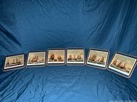 Full display of all six antique coasters arranged in a line on a blue fabric background. Each coaster features different detailed naval ship illustrations.