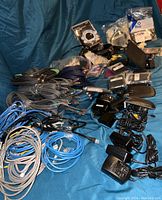 Wide view of all assorted cables, power adapters, phone holsters, and small accessories laid out on blue fabric.