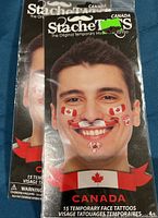 Front photo of one of the packages showing man with several Canada themed temporary tattoos on his face including flags and maple leaves. Package states 15 temporary face tattoos.