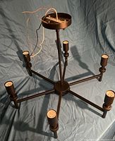 Six-arm metal chandelier with black finish on blue fabric background, showing wiring and ceiling mount canopy.