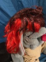 Red and black synthetic wig shown draped over a plush toy.