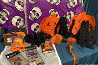 Photo showing various Halloween party decorations including purple skull and pumpkin tablecloths, black cats, black haunted house, pumpkins, bouquets of black roses and tableware