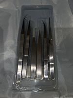 Photo of 5 metallic tweezers in a plastic tray, featuring various tip shapes for precision tasks.