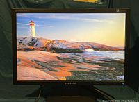 Samsung SyncMaster 2043NW 20-inch monitor powered on displaying a vibrant image of a lighthouse and rocky coastline indicating it is in working condition.
