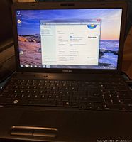 Toshiba laptop opened showing system information on screen, Windows 7 OS desktop visible