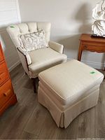 Side view of beige upholstered armchair and matching ottoman, with decorative throw cushion on the chair