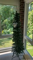 Full view of the pencil Christmas tree standing in a corner near windows, showcasing its height and shape.