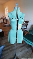 Front view of the adjustable dress form mounted on metal stand, covered in teal textured fabric with defined bust, waist and hips.