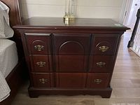 Front view of the dark brown wood/composite dresser showing three drawers with metal handles and decorative paneling.