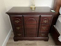 Front view of wood composite dresser with three drawers, metal handles, dark finish and polished top surface.