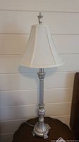 Full view of metal based lamp with fabric white shade showing detailed base and shade shape.