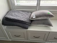 Two gray throw cushions with small white dot pattern on one side and solid gray on the other stacked on folded gray quilted bed coverings with star pattern.