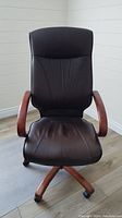 Front view of the black leather office chair showing the seat, backrest with stitched pattern, and wooden armrests and base.