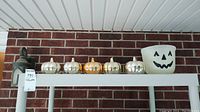 Five small decorative pumpkins and one plastic bucket with jack-o'-lantern face on a shelf