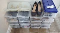 Stack of multiple plastic boxes containing shoes with two different pairs placed on top of the boxes.