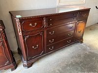 Front view showing the sideboard with seven drawers and two cupboards, metal fittings, decorative carving, and wood veneer finish.