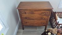 Front view of wooden sideboard showing three drawers and wooden knobs, placed on the floor against a white wall.