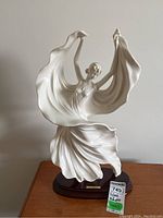 Front view of signed white porcelain statuette depicting a dancing woman in flowing dress on wooden base with nameplate and sale tag.