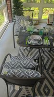 Photo showing metal dining table with two chairs, cushions on seats and back, set with dishes (not included)