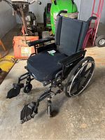 Side view of black Invacare 9000XT collapsible wheelchair showing padded seat and backrest, armrests, large rear wheels, foldable footrests and attached carry bag.