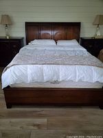 Front view of the queen size dark wood bed frame with bedding and mattress on it