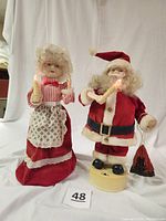Pair of Mr. and Mrs. Claus vintage Christmas figures on white backdrop, showing Mr. Claus in red suit with candle and sack, Mrs. Claus in apron and bonnet holding candle.