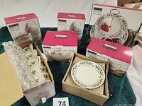 Photo showing 8 mugs in original box alongside other boxed dishes and loose saucers