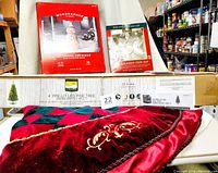 Photo showing boxed Wondershop lit fabric snowman, boxed Kurt S. Adler Capiz star tree topper, box of pre-lit artificial pine tree, and velvet burgundy tree skirt spread out.