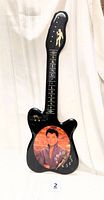 Full view of the guitar-shaped clock showing the silhouette of Elvis on the top, guitar neck with 'KING ELVIS' text and musical notes, and the large picture of young Elvis with clock face on the body.