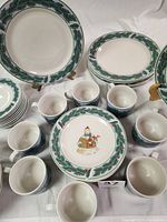 Top view showing large dinner plates with green holly borders, some luncheon plates, and mugs arranged around.