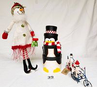 Wide shot of the three items: snow lady figurine, nested penguin containers, and two snowmen bicycle figurines