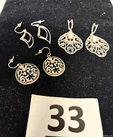 Three pairs of sterling silver pierced earrings shown on black background: filigree round with rhinestone, oxidized filigree teardrop with pearl, stylized silver pair