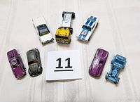 Seven vintage diecast cars arranged on fabric background, showing variety and wear.