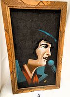 Front angled photo showing Elvis wearing a blue shirt with an orange neck cloth, tear running down cheek, black velvet background, carved wood frame with geometric pattern.