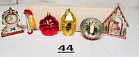 Front view of six vintage Christmas ornaments displaying various shapes and colors, including red glass, acrylic clock, wood trombone, and clear plastic snowman decorations.