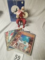 Photo showing Story Teller Santa figurine sitting on a wooden chair with red book, four Little Golden Books laid in front, and original box with Santa sleigh design behind.