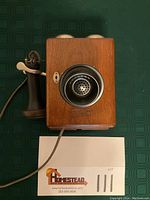 Full front view of antique Western Electric telephone with wooden case and candlestick handset lying to the side, with cord attached.