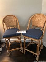 Two bamboo tall counter bar stools with navy blue custom cushioned seats with small white dots, placed on dark flooring and positioned in front of a light wall.