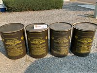 Four cylindrical vintage painted metal storage containers with lids, dark color with yellow civil defense survival supply text for drinking water.