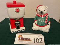 Photo of both Coca Cola cookie jars together on green surface.