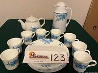 Photo showing the full set of eight swirl rim dinner plates, eight coffee cups, one teapot, and one Corning Thermique coffee server with blue rose decoration.