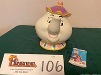 Photo of Mrs. Potts ceramic cookie jar alongside unopened 1992 ProSet collector card pack with lot number sign visible.