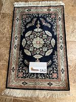 Full view of the entire rectangular handmade area rug showing the central floral medallion, patterned borders, and fringed ends.